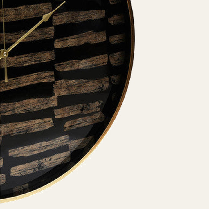 Soren Wall Clock close-up: round black glass face with distressed bronze horizontal brushstroke pattern, thin gold metal rim and gold clock hands
