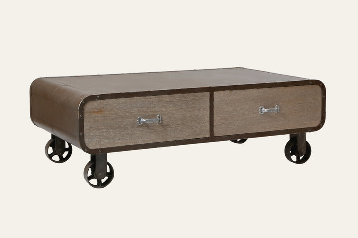 Stellan Two Drawer Coffee Table with low rectangular brown metal frame, rounded riveted corners, two weathered wood drawer fronts with silver metal handles, on industrial metal caster wheels