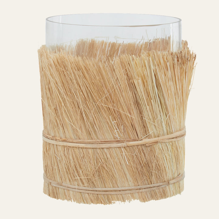 Velora Candle Holder — clear glass cylinder wrapped in natural straw with two thin binding bands and a fringed straw top edge