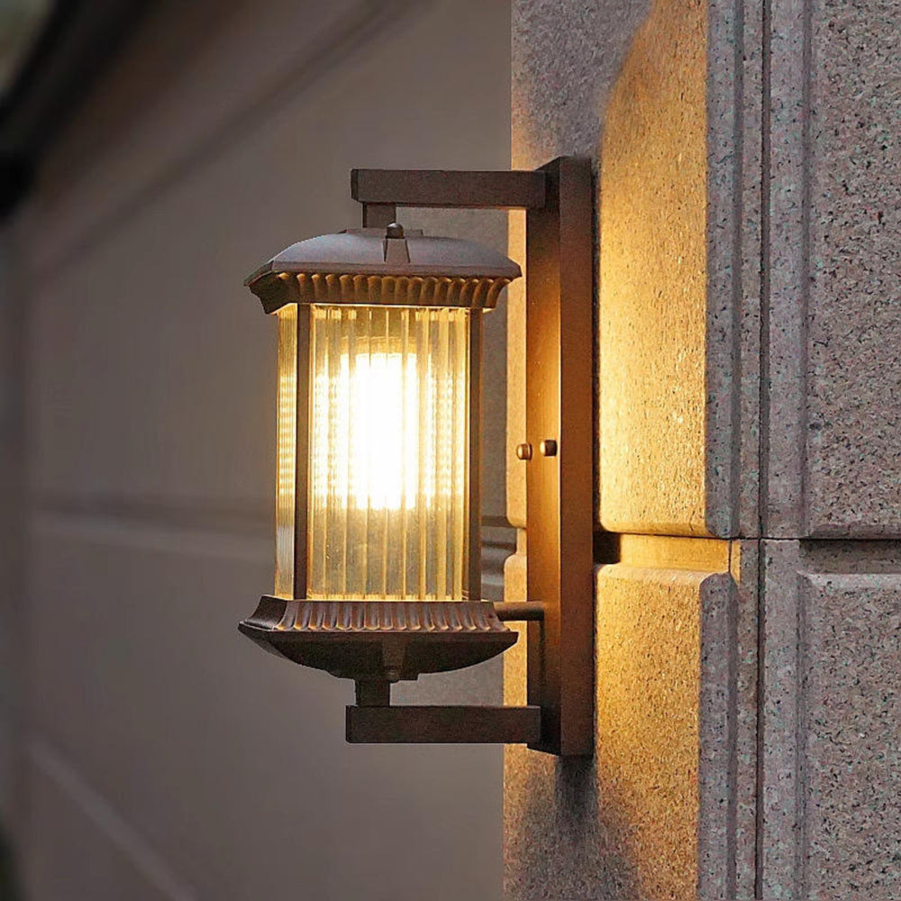 Black outdoor wall lantern illuminated with a warm glow beside an entrance