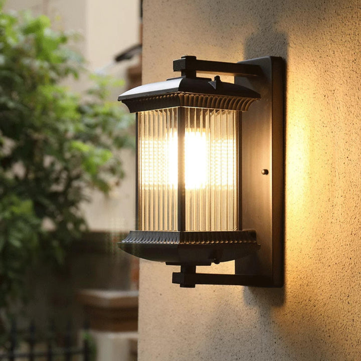 Black outdoor wall light installed beside a garden entrance with yellow flowers